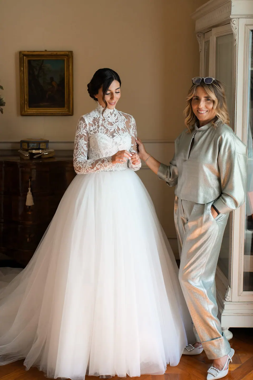 Bride in her gown with a woman in a silver suit in a room