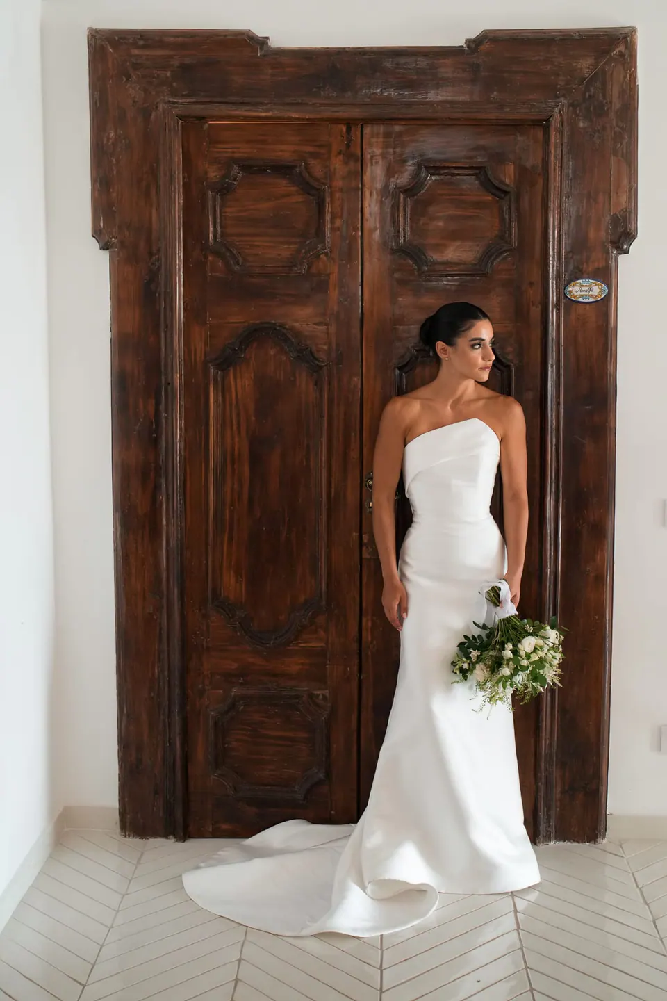 Bride in front of a carved wooden door, holding her bouquet.