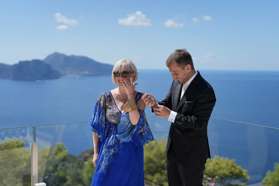 Il papà della sposa appunta un fiore sull'abito della mamma, Capri alle spalle.