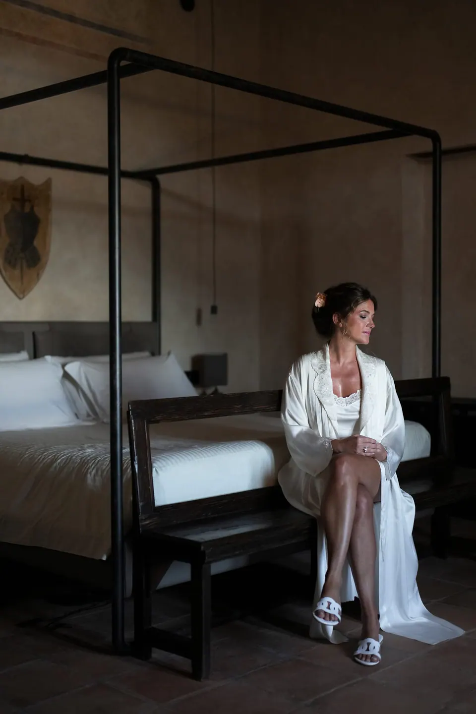 Sposa in vestaglia seduta accanto al letto a baldacchino nella suite del castello.