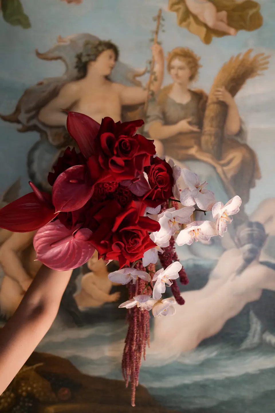 Bouquet rosso scuro contro un soffitto affrescato.