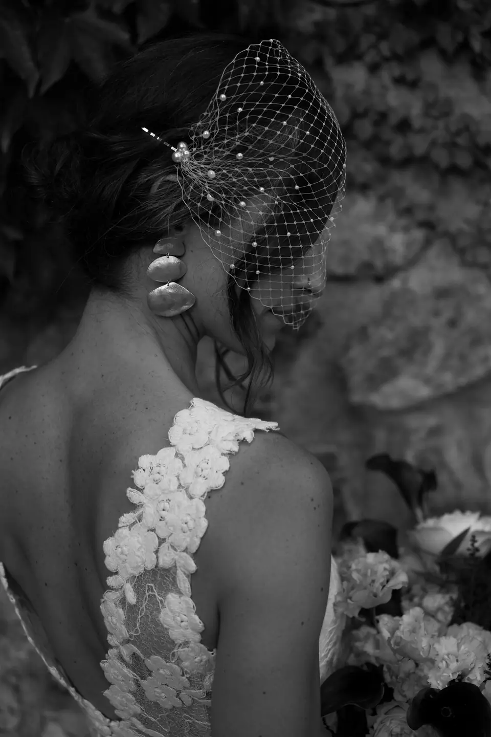 Black and white close-up of the lace back of the dress and the birdcage veil.