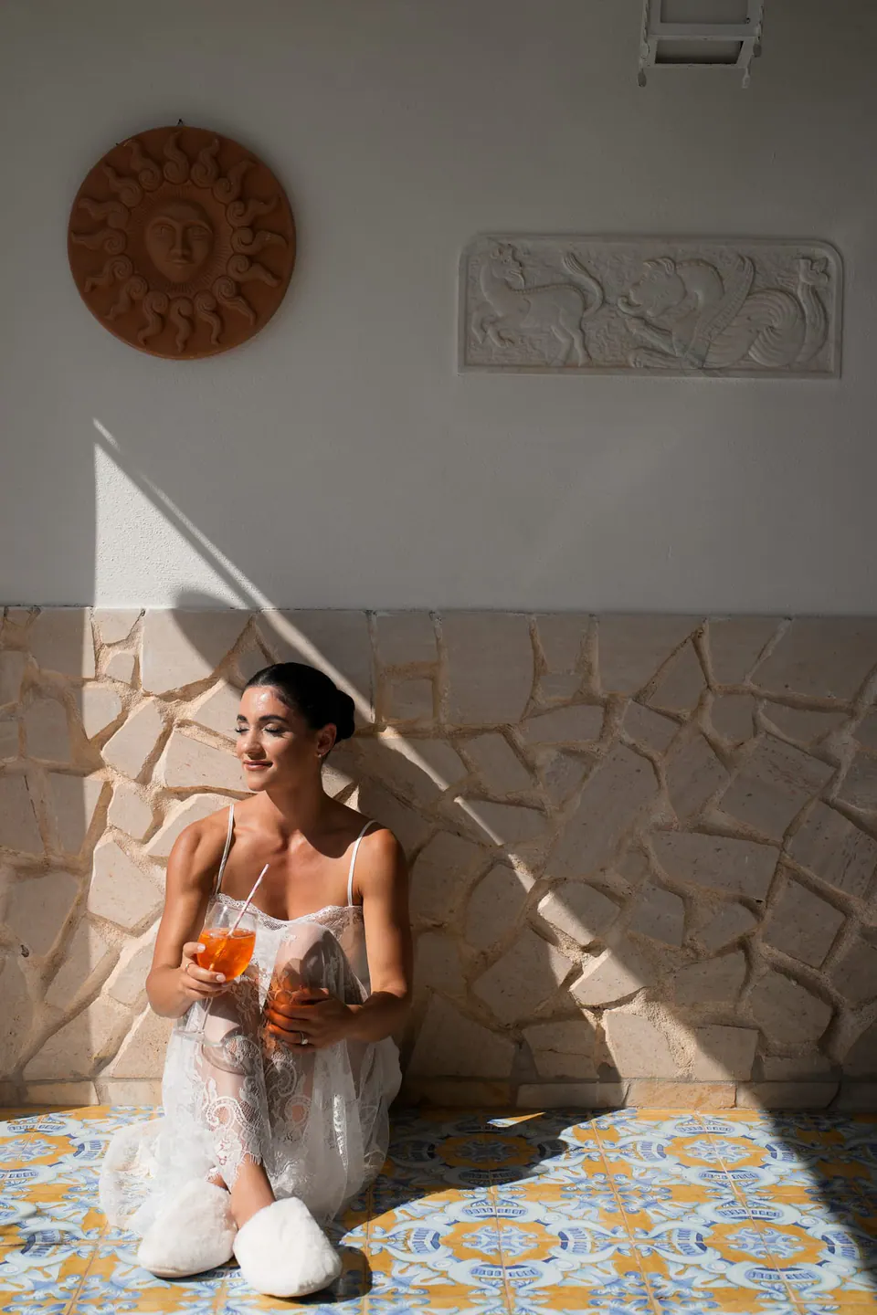Bride seated on a majolica floor in the sun, a spritz in hand.