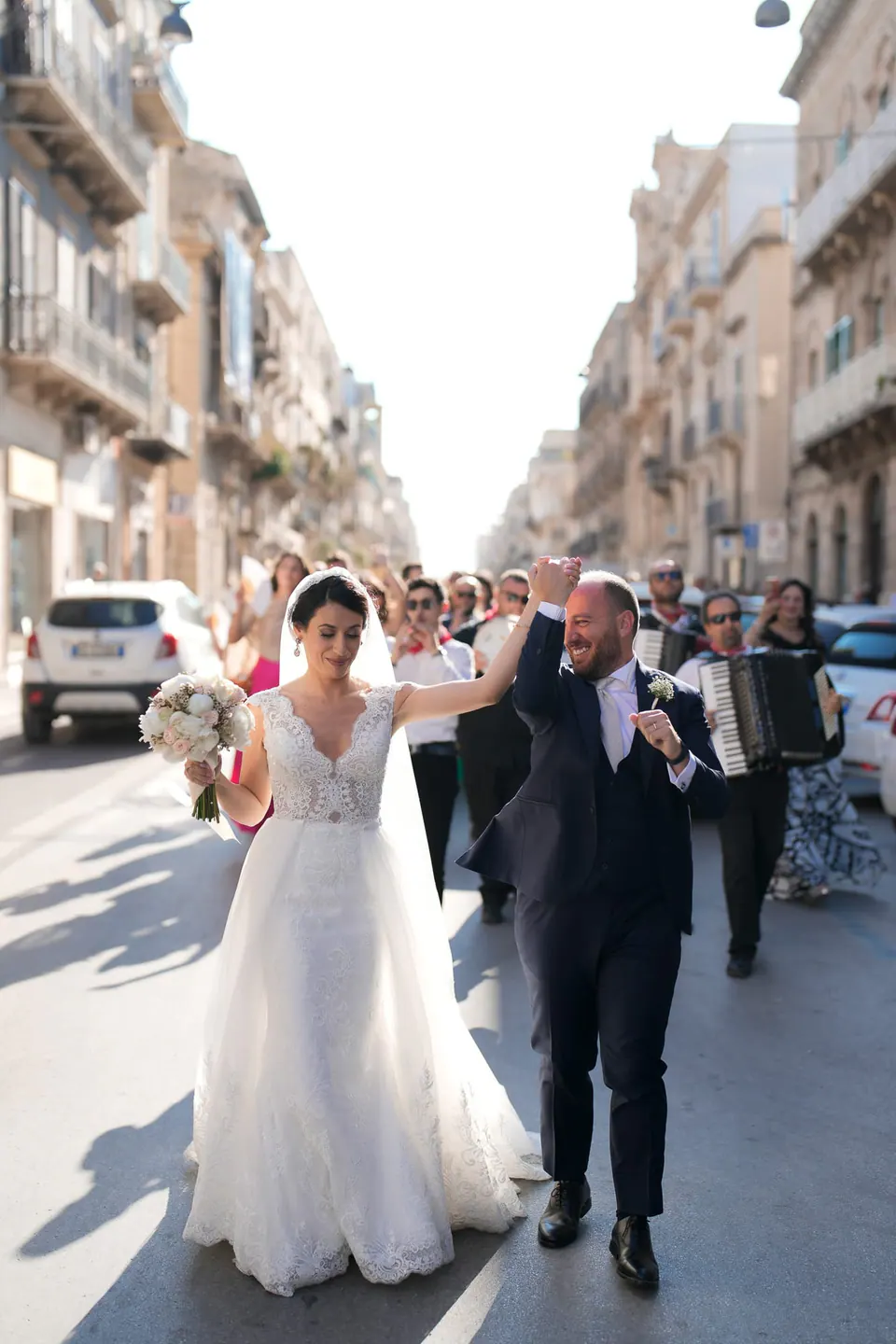 Bride and groom walking together in historic town, candid wedding photography Sicily.