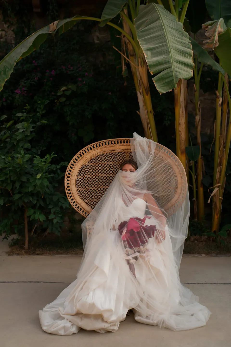 Sposa sotto il velo nella poltrona a pavone, il bouquet in grembo.