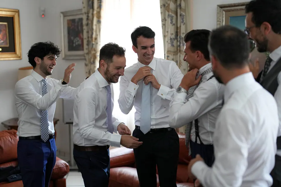 Groomsmen sharing laughter while helping the groom get ready, candid storytelling moment.