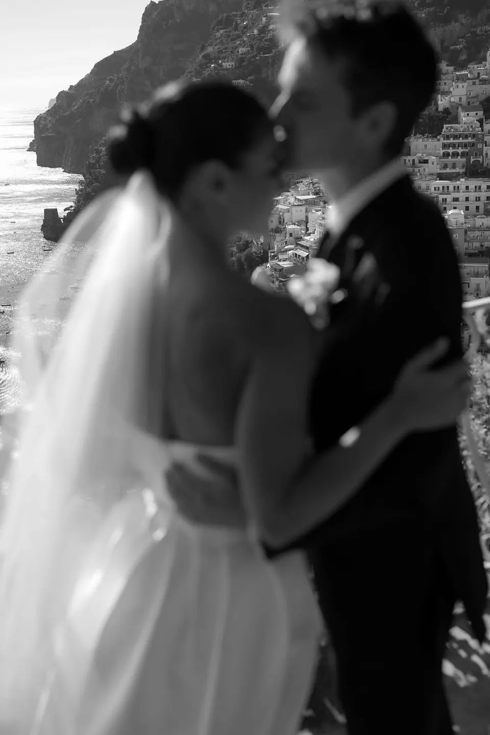 Black and white photo of the couple embracing, the bride's veil lit from behind.