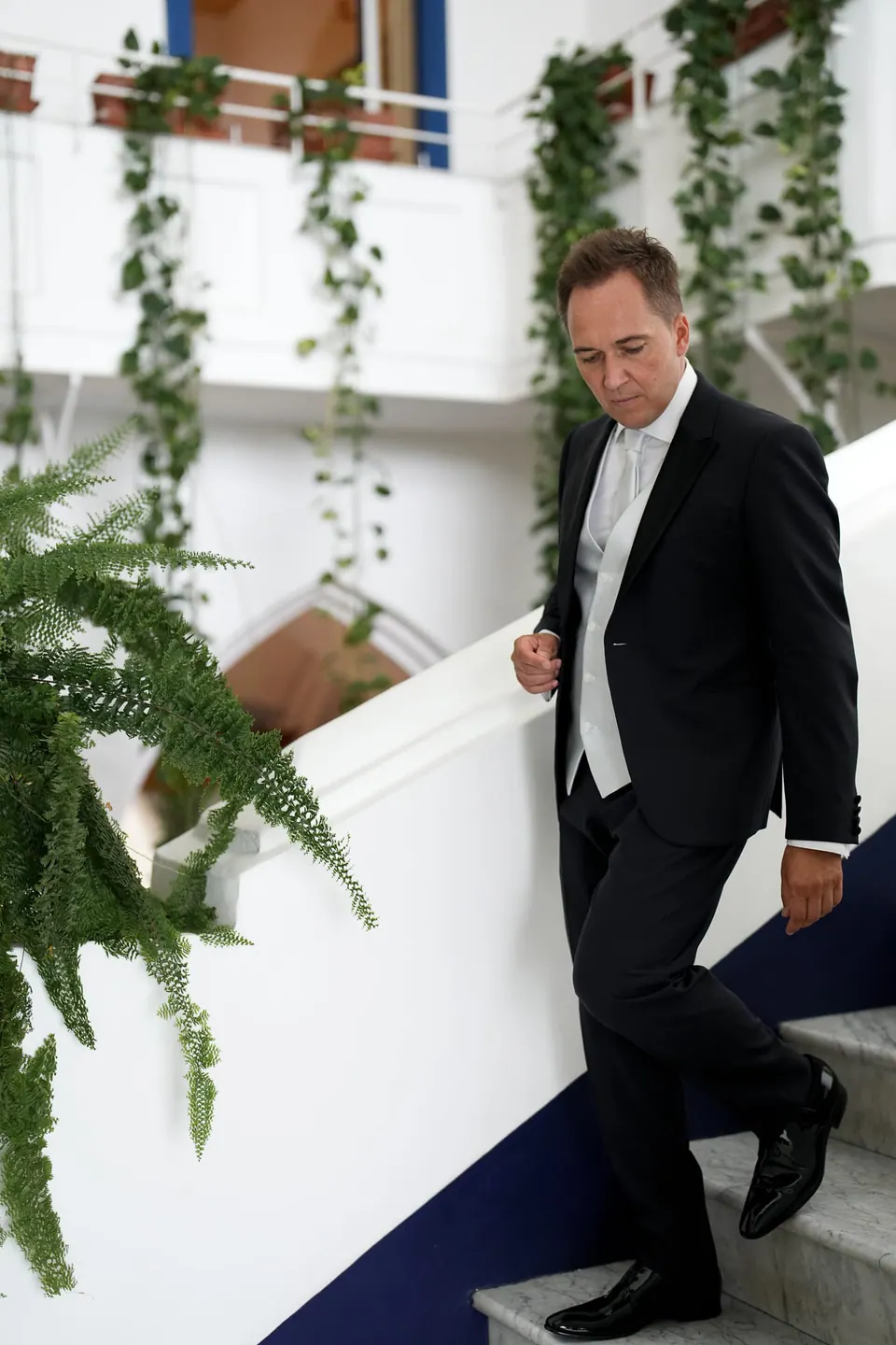Groom walking down a staircase among green plants