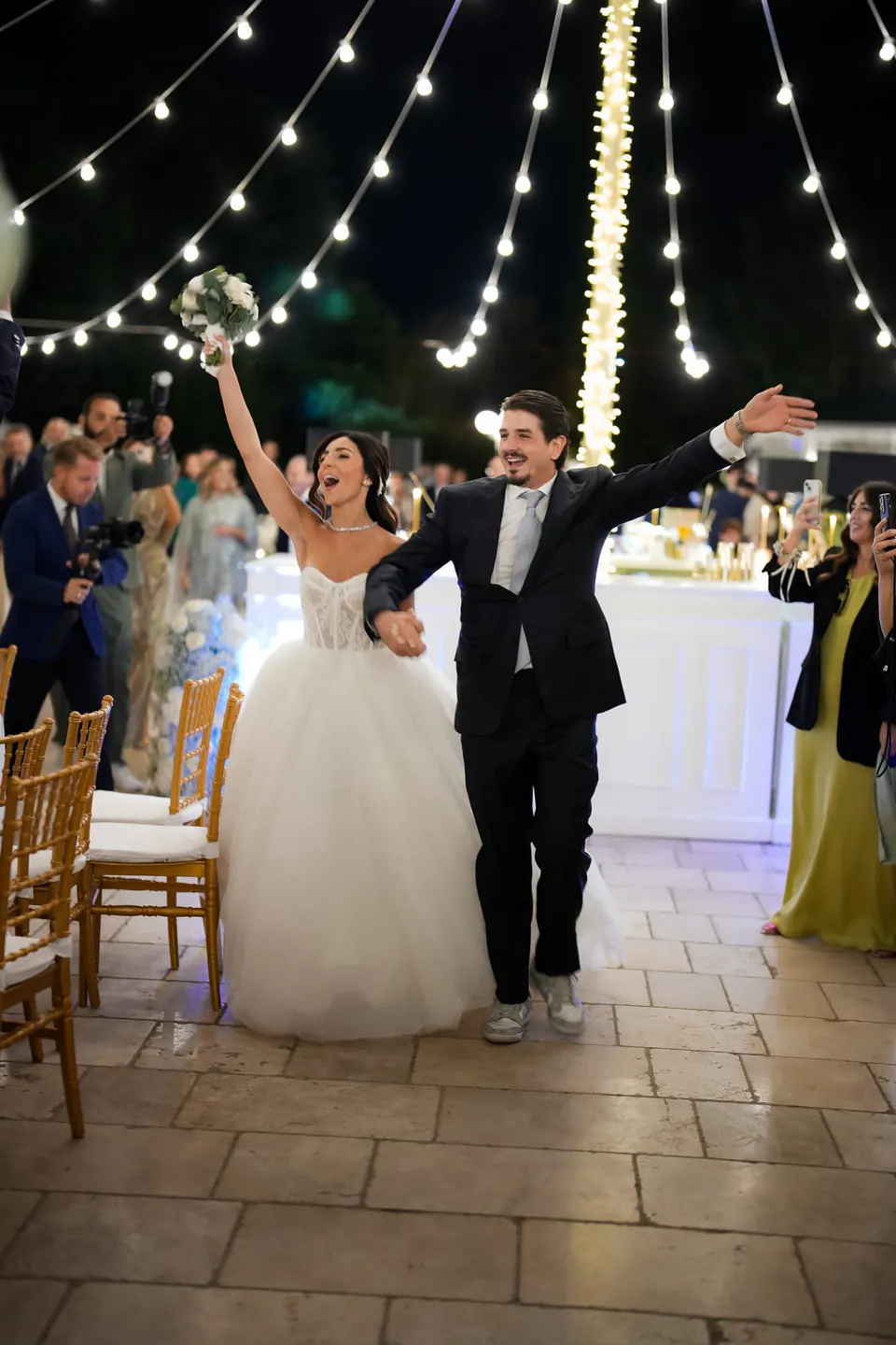 Bride and groom walking hand in hand under the lit arches of Tenuta San Domenico at night.