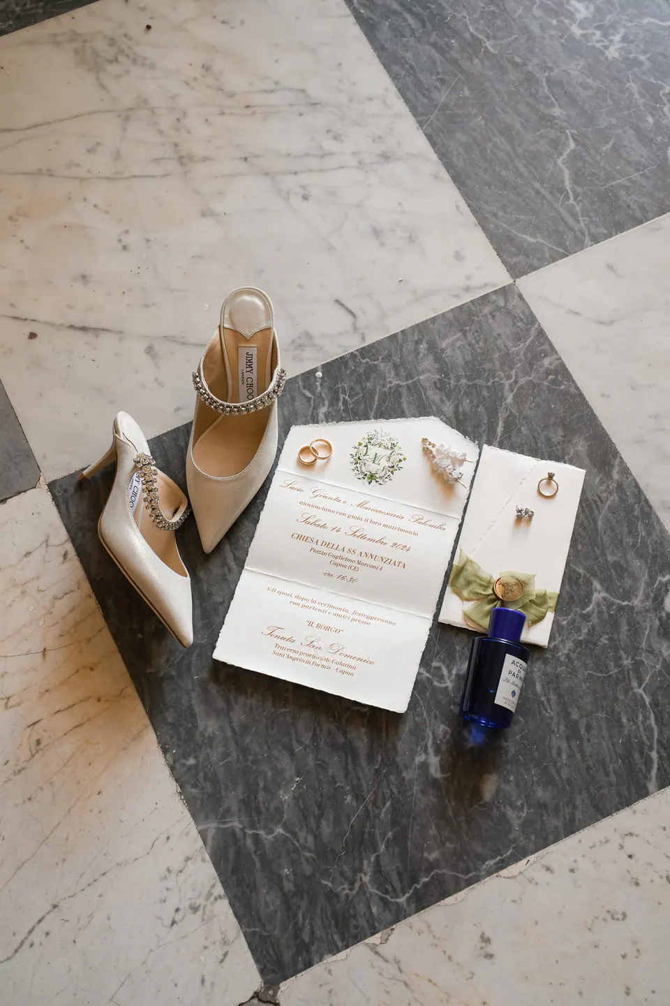 Wedding invitations, perfume and jewellery laid out on a neutral background.