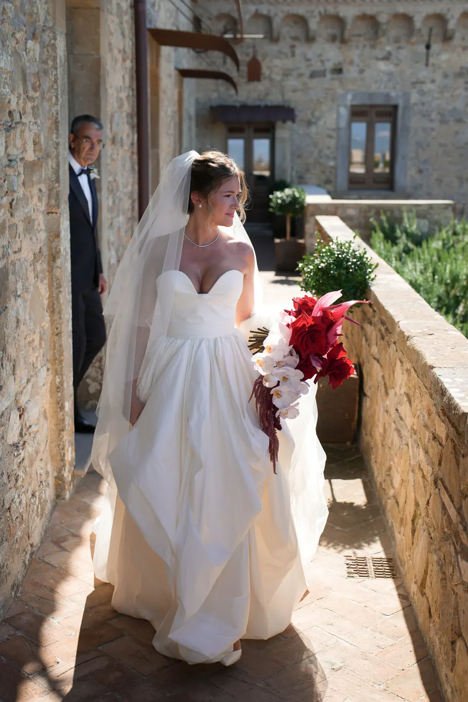 Sposa lungo il balcone del castello con il bouquet rosso.