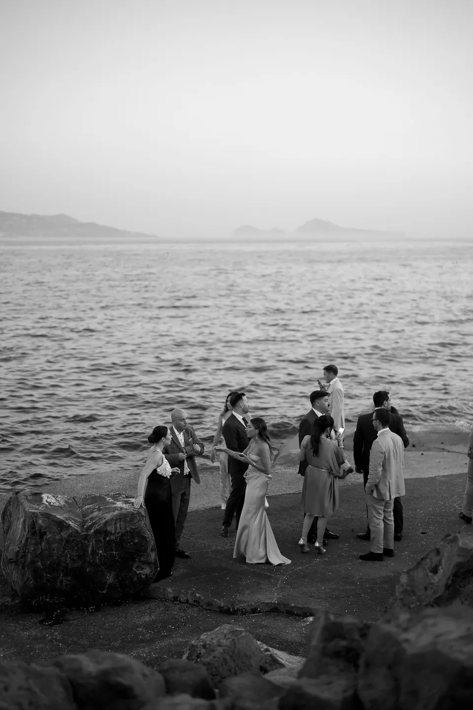 Schwarzweißfoto von Paar und Freunden auf den Felsen am Meer.