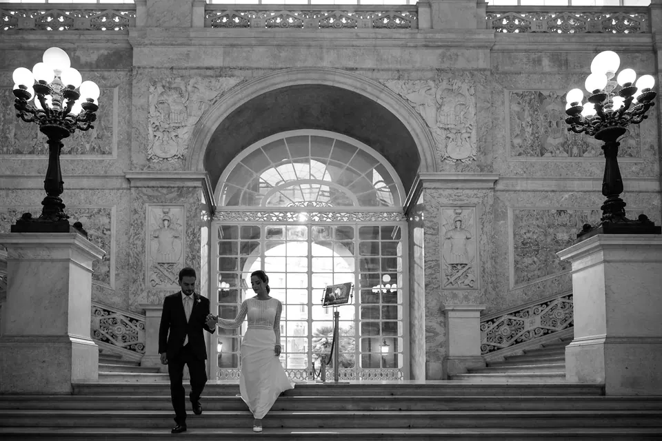 Black and white photo of the couple walking out through a grand arched gateway with ornate lamps.