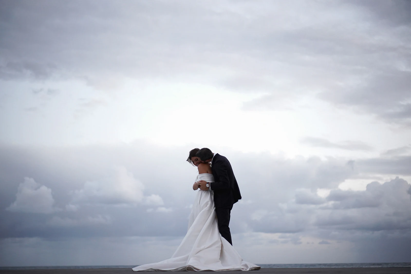 Bride and groom embracing by the sea under a cloudy sky in Amalfi.
