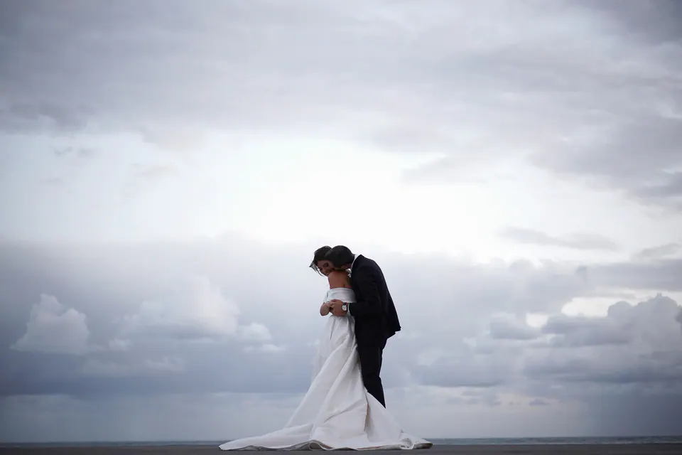 Bride and groom embracing by the sea under a cloudy sky in Amalfi.