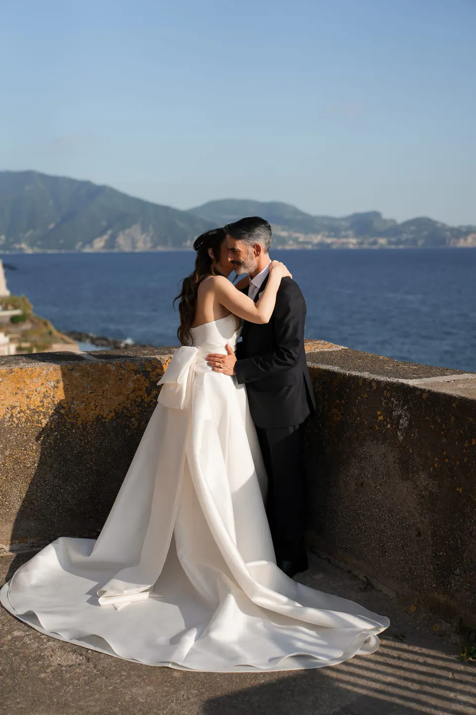 Los novios abrazados sobre un muro de piedra sobre el mar.
