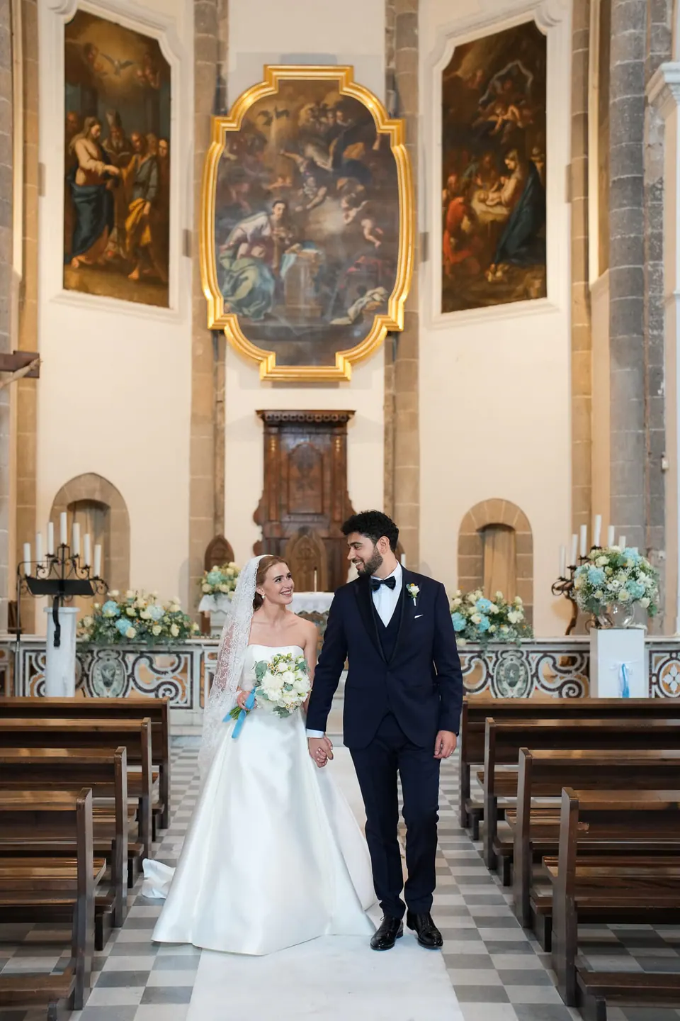 Das Brautpaar geht durch die Barockkirche, hinter ihnen der vergoldete Altaraufsatz.