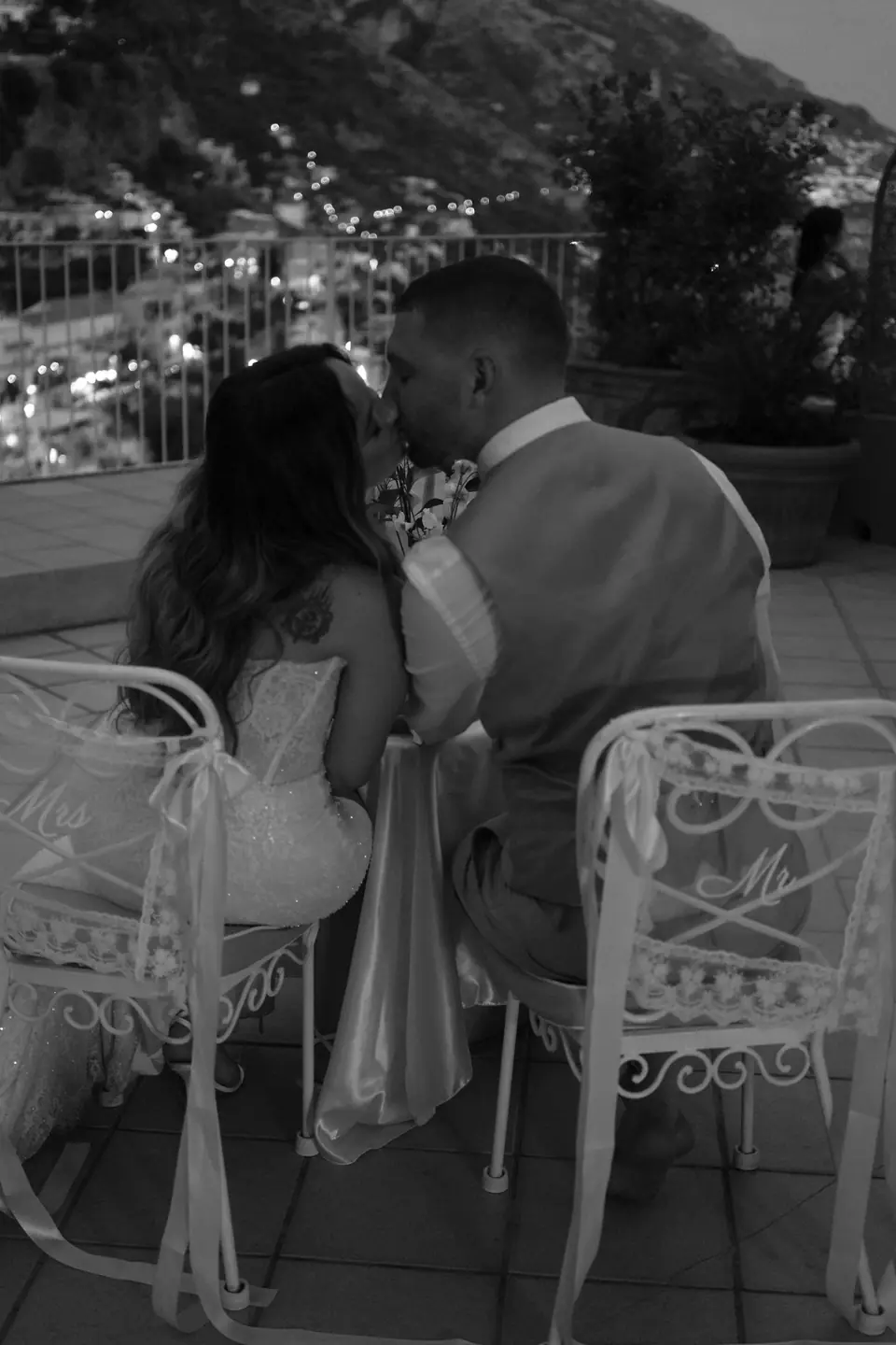Black and white photo of the couple at a table at night, the lights of Positano below.