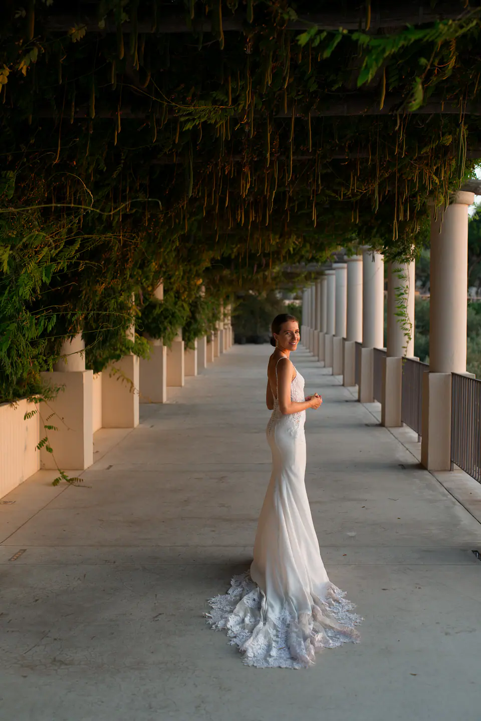 Bride standing alone under a long pergola with columns.