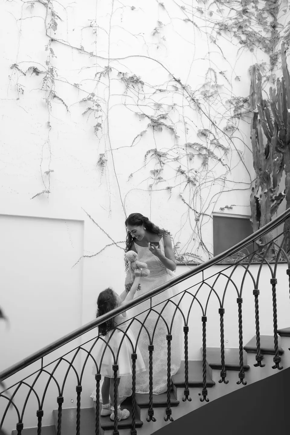 Black and white photo of the bride on the wrought-iron staircase, shadows of plants on the wall.