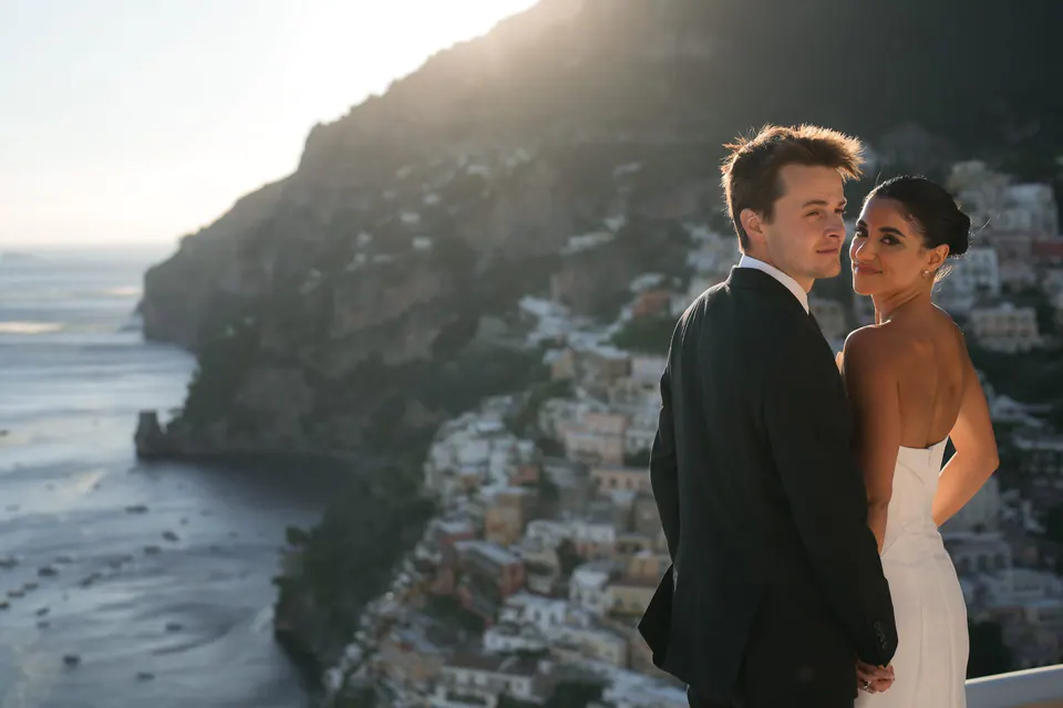 Bride and groom close together, the cliffs of Positano behind them.