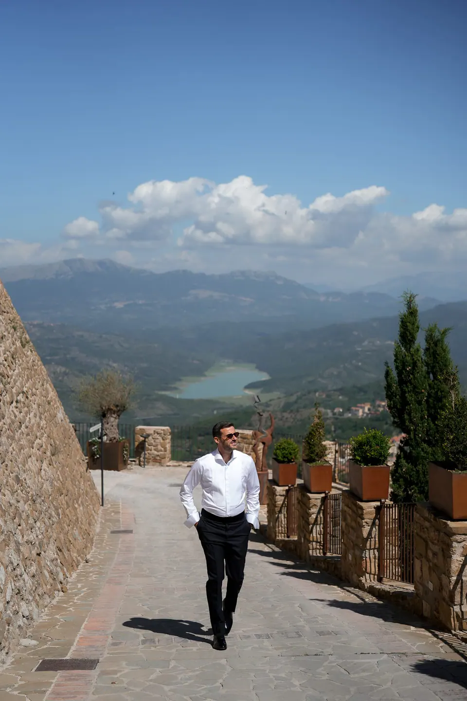 Lo sposo lungo il sentiero del castello, alle spalle le colline verdi e il lago del Cilento.