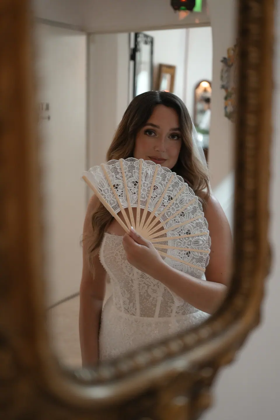 Bride holding a lace fan, reflected in an old gilded mirror.
