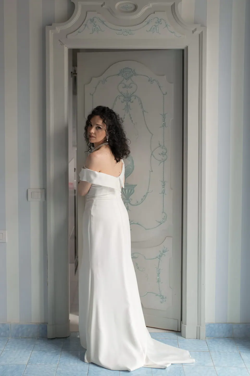 Bride in a minimal gown standing in the doorway of Villa Ortensia D'Avalos.