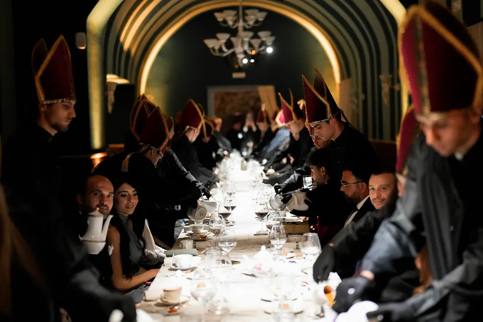 Invitados en una larga mesa de cena con artistas disfrazados.