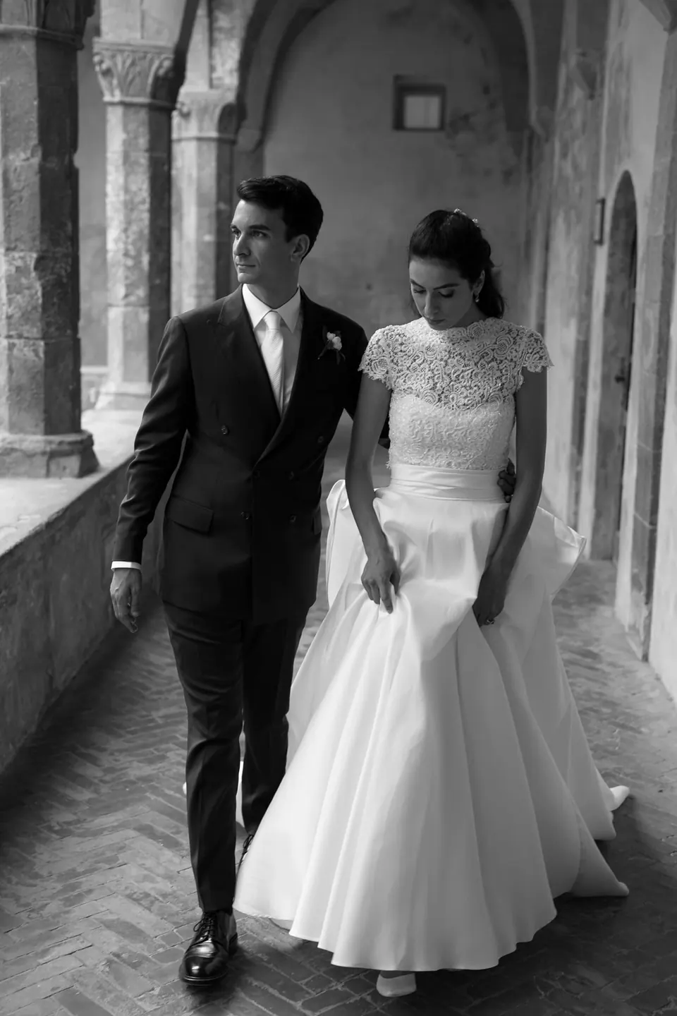 Black and white photo of bride and groom walking along the cloister of San Francesco