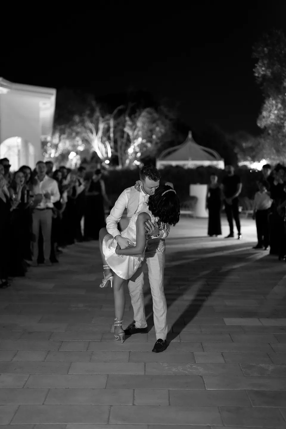 Première danse en plein air la nuit, en noir et blanc, les invités en cercle autour du couple.