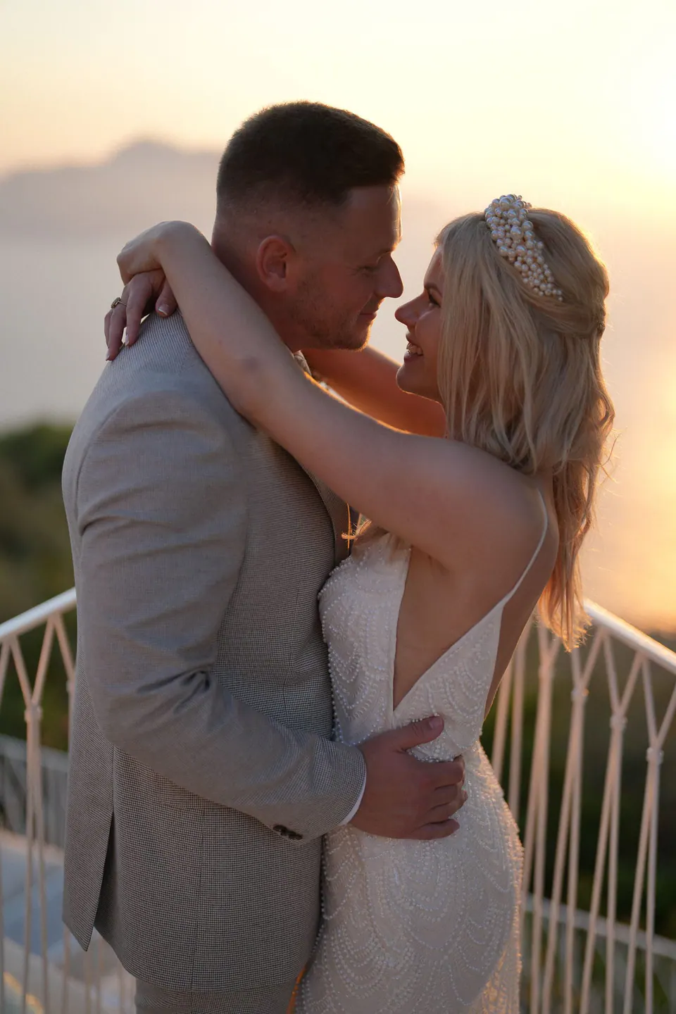 Bride and groom embracing at a railing at sunset
