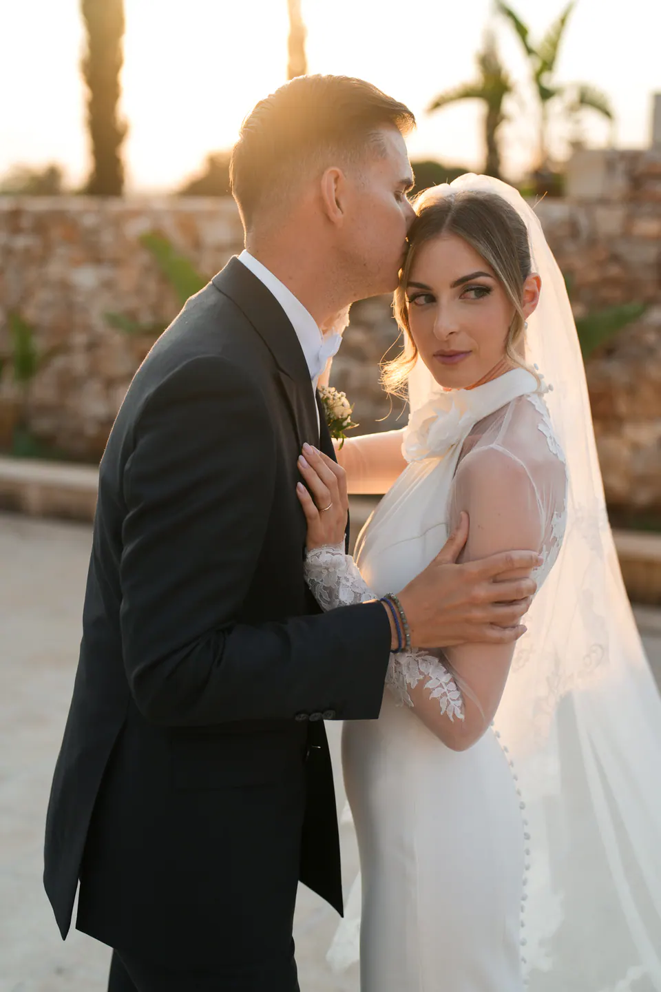 Lo sposo che bacia la fronte della sposa nella luce dorata del tramonto salentino.