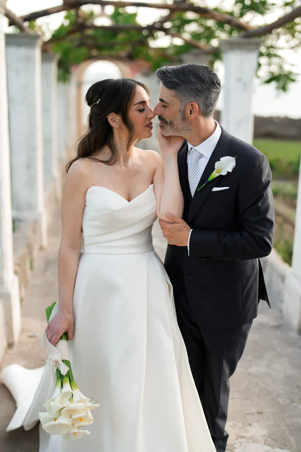 Los novios sonrientes y muy juntos bajo la pérgola.