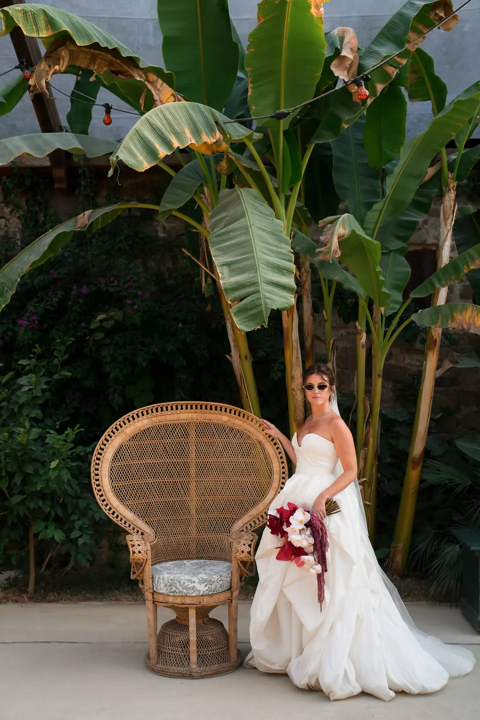 Sposa accanto alla poltrona a pavone con un bouquet di fiori rosso scuro.
