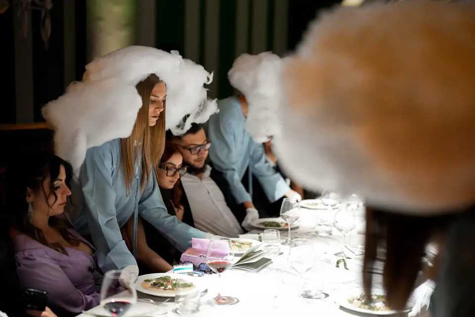 Invitados en la cena, con un artista con peluca blanca en primer plano.