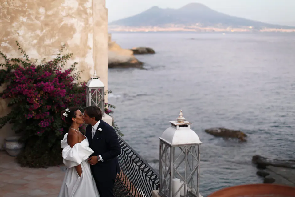 Bride and groom kissing on the terrace among bougainvillea, Mount Vesuvius across the Gulf of Naples.