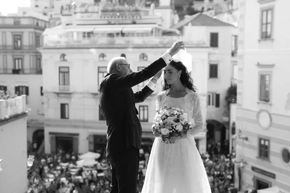 Black and white photo of the father of the bride arranging her veil in the crowded piazza of Amalfi.