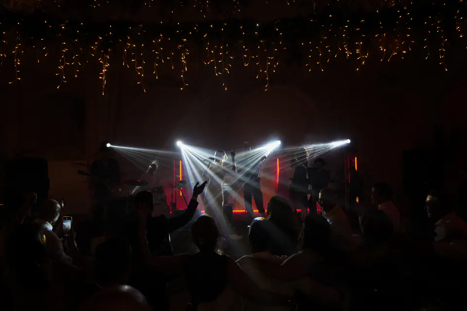 Le luci del palco che tagliano il buio mentre gli invitati ballano alla festa.