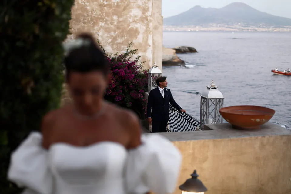 Bride softly out of focus in the foreground, the groom waiting on the terrace with Vesuvius behind.