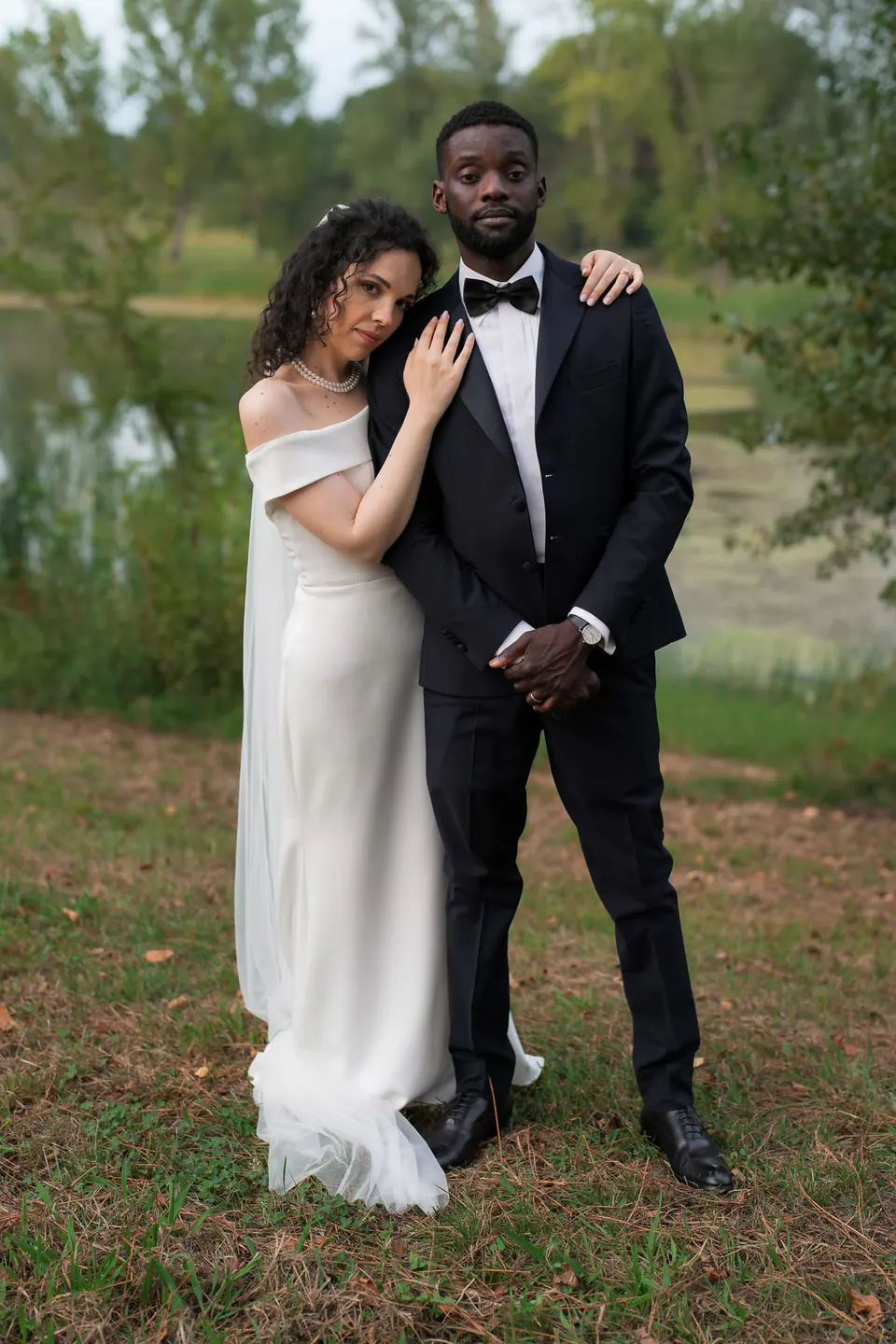 Los novios juntos en el césped del parque de la villa, con árboles detrás.