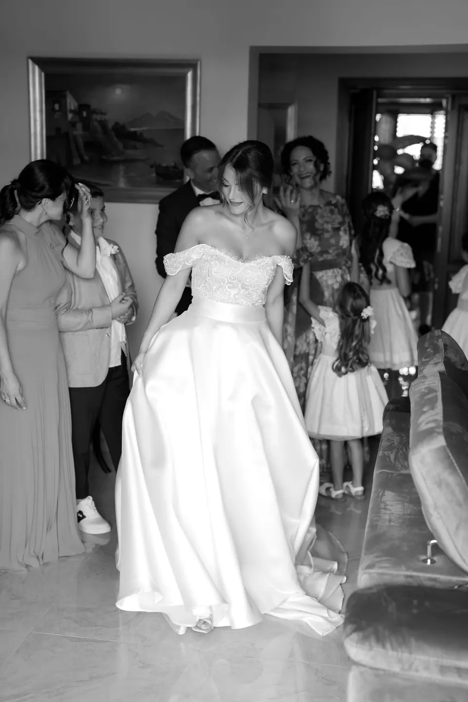 Black and white photo of the bride in her dress with her family in the room