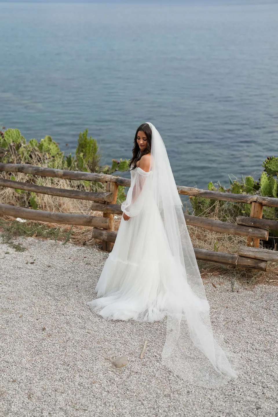 Bride standing on a garden path overlooking the sea, calm and luminous atmosphere.