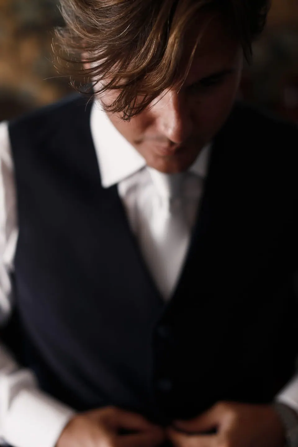 Groom buttoning his waistcoat before the ceremony.