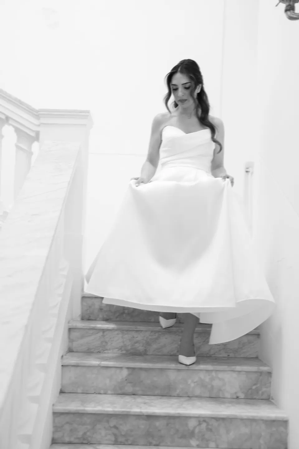 Foto en blanco y negro de la novia bajando una escalera blanca.