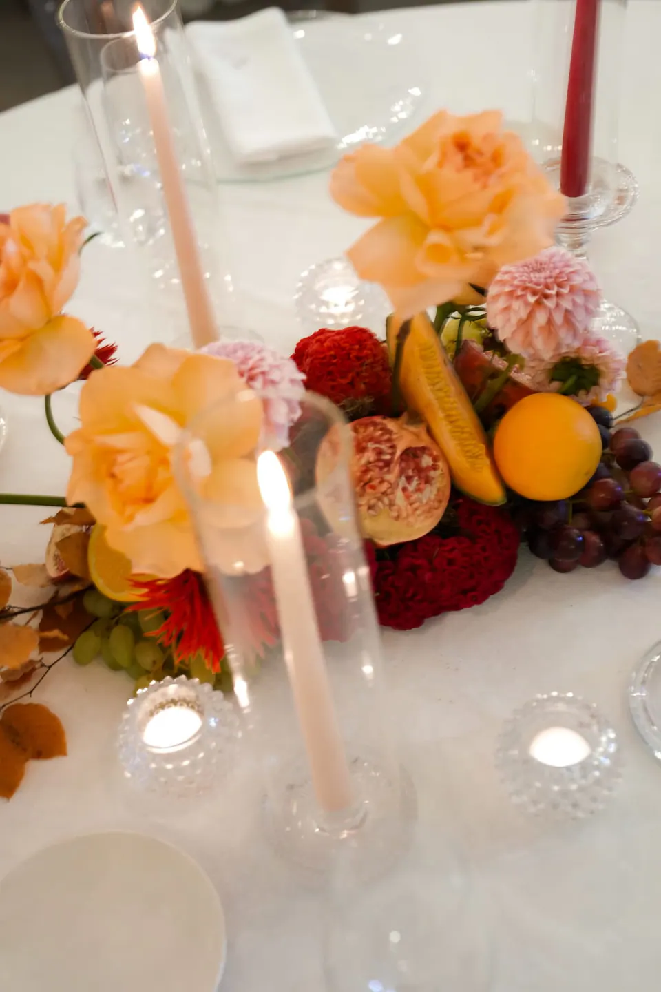 Centrotavola di rose color pesca, frutta e candele alte.