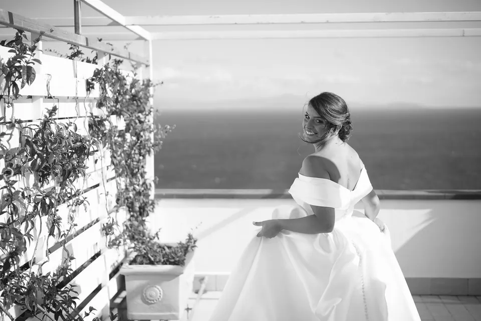 Black and white photo of the bride seated on the terrace, the sea beyond.