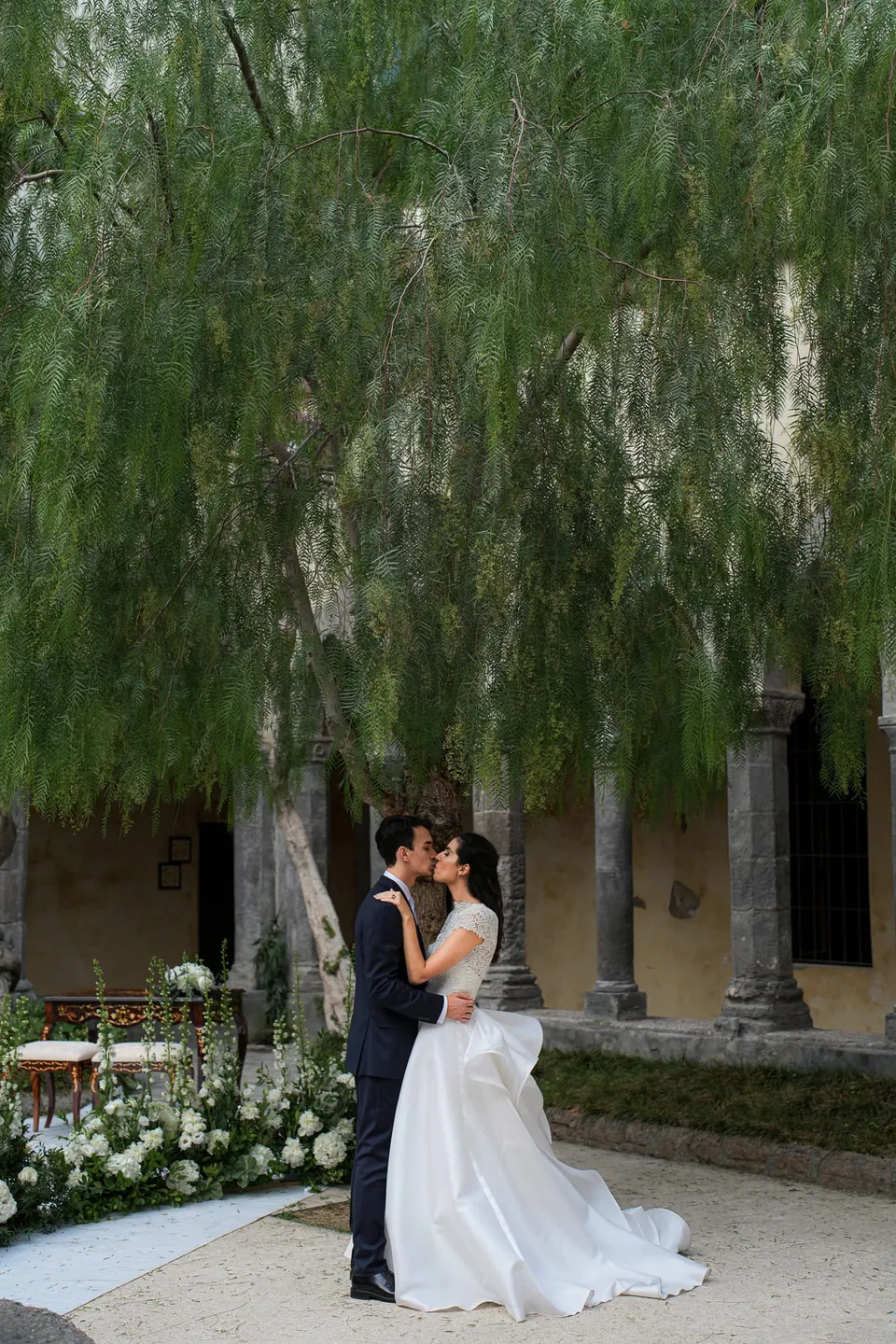 Bride and groom kissing in the cloister garden under a weeping tree