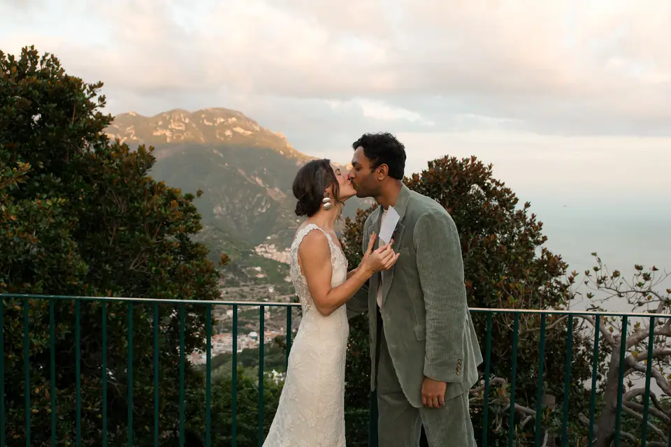Couple kissing during the vow exchange, the mountains of the coast behind.