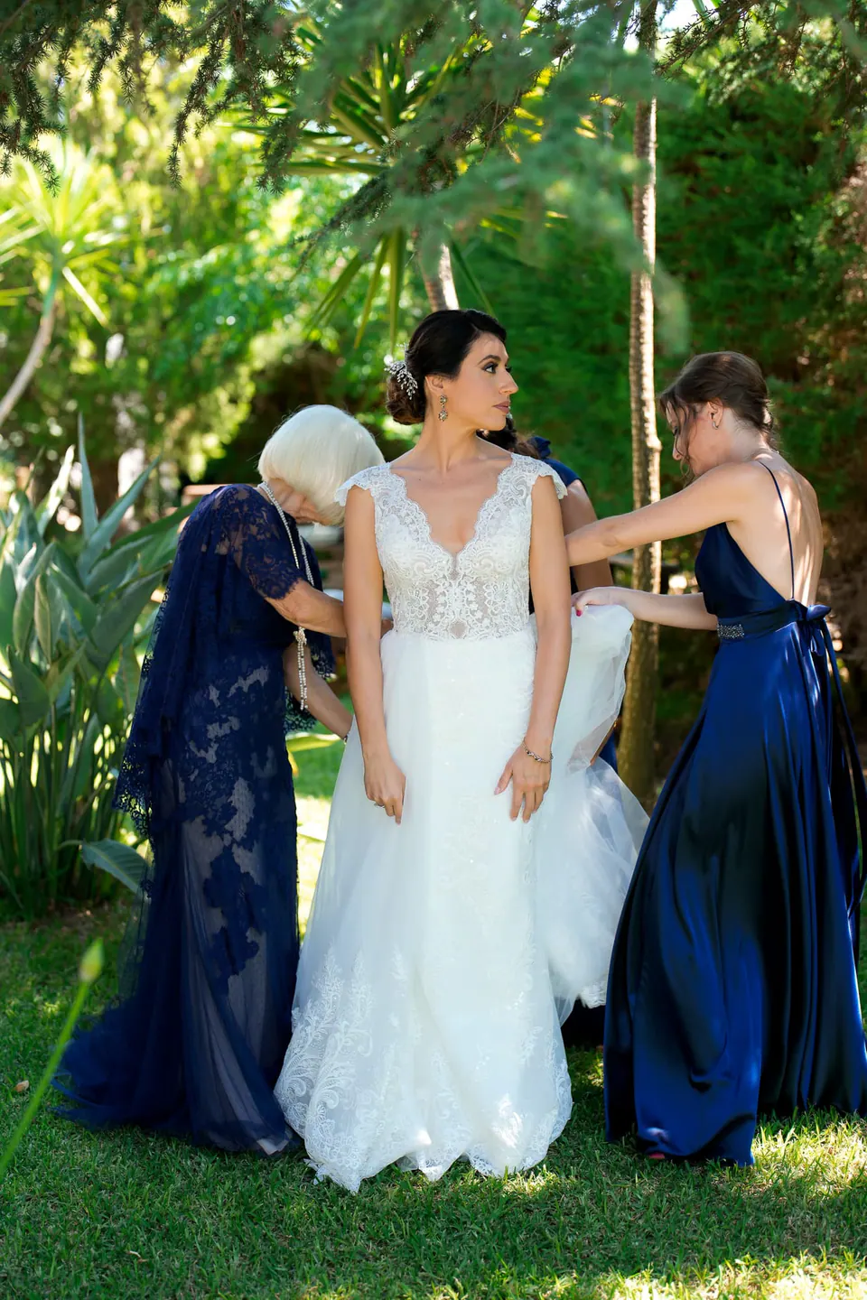 Women fastening the bride's dress in the garden